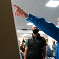 Scholar pointing out a section of poster to guest, both wearing masks.